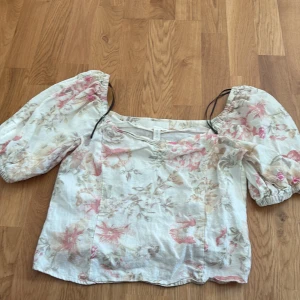 Blommig linnetopp från H&M - Supersöt blommig linnetopp från H&M i ljusa toner med puffiga trekvartsärmar och romantiskt mönster i rosa, beige och grönt. Toppen har en luftig passform och är perfekt för varma dagar. Tillverkad i en skön linneblandning.