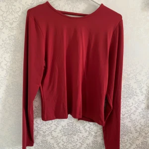 Röd långärmad topp med snörning - Snygg röd långärmad topp med öppen rygg och cool snörningsdetalj baktill. Tunn och mjuk i materialet, perfekt för dig som vill sticka ut lite extra. Enkel att styla med både jeans och kjol.