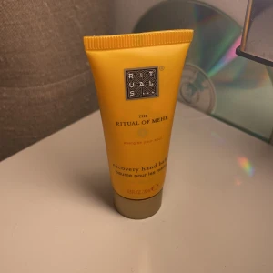 Rituals The Ritual of Mehr hand balm - En gul tub med The Ritual of Mehr recovery hand balm från Rituals. Tuben rymmer 20 ml och har en smidig, kompakt design som är perfekt att ha med i väskan. Doften är fräsch och energigivande, och krämen är återfuktande för händerna.