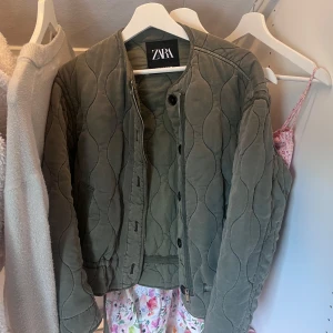 Quiltad grön jacka från Zara XS - Säljer en quiltad, olivgrön jacka från Zara i storlek XS. Jackan har rund halsringning, dragkedja och knappar framtill samt elastisk nederkant. Använd 2 gånger! Som ny