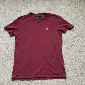 Vinröd t-shirt från Lyle & Scott - Snygg vinröd t-shirt från Lyle & Scott med klassisk gul broderad logga på bröstet. T-shirten har rund halsringning och korta ärmar. Tillverkad i mjuk bomull som känns skön mot huden. Perfekt för en clean och stilren look.