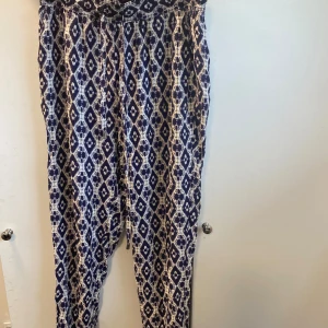 Mönstrade byxor Saints and Mortals XS - Snygga byxor från Saints and Mortals i blått och vitt med grafiskt mönster. De har resår i midjan och mudd vid benslut. Lätta och sköna, perfekta för chill dagar eller när du vill sticka ut lite extra. Börjar bli Liiite slappa i resåren, men går att knyta till 
