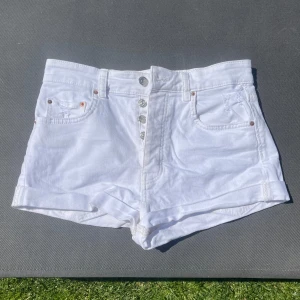 Vita högmidjade jeansshorts - Snygga vita högmidjade jeansshorts med uppvikta benslut och klassisk femficksdesign. Shorts med knappgylf och silverfärgade knappar. Perfekta för varma dagar och enkel att matcha med allt.