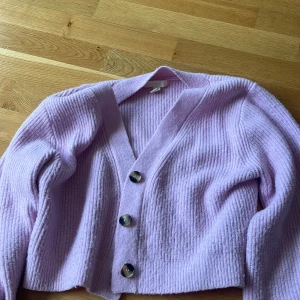 Ljuslila stickad kofta med knappar från H&M - Superfin ljuslila stickad kofta med tre stora knappar framtill. Koftan är ribbad och har en croppad passform med långa ärmar. Perfekt att slänga över en topp för en chill och trendig look.