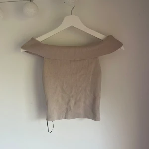 Beige offshoulder topp från H&M - Snygg beige offshoulder topp från H&M i ribbad bomullsmix. Toppen har en bred, vikt krage som ger en cool och trendig look. Perfekt att styla med jeans eller kjol för en clean vibe.