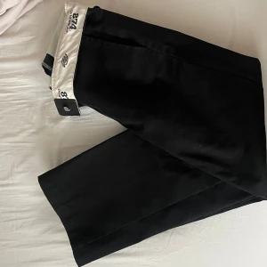 Dickies 874 byxor - Klassiska svarta Dickies 874 byxor med rak passform och stilren look. Byxorna har en hög midja och är tillverkade i slitstark bomullsblandning. Perfekta för dig som gillar streetwear eller vill ha en clean stil.