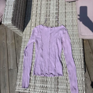Ljuslila ribbad topp från Gina Tricot - Supersöt ljuslila långärmad topp från Gina Tricot med ribbad struktur och vågiga kanter. Figurnära passform och dekorativa sömmar framtill ger en trendig look. 