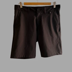 Svarta shorts Peak Performance 30 - Snygga svarta shorts från Peak Performance i klassisk modell med normal passform. De har fickor i sidorna, bälteshällor och stängs med knapp och dragkedja. Perfekta för sommardagar när du vill ha en clean och stilren look.