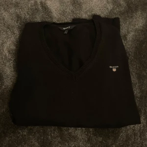 Svart v-ringad tröja från GANT - Klassisk svart v-ringad tröja från GANT med liten broderad logga på bröstet. Perfekt för en stilren och enkel look.