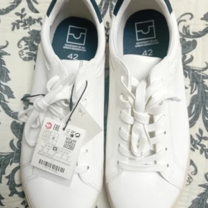 Vita sneakers med snörning - Fräscha vita sneakers från Movement of An med klassisk design och snörning. Skorna har rund tå och platt sula, perfekta för en stilren look. Märket syns på innersulan och de är i syntetmaterial.