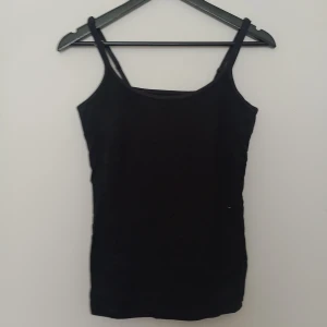 Svart linnetopp - En enkel och stilren svart linnetopp från Stockh LM. Toppen har smala axelband och rak halsringning, perfekt att matcha med jeans eller kjol. Gjord i ett mjukt material som känns skönt mot huden.