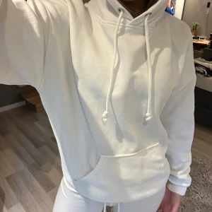 Vit hoodie med ficka - Säljer en klassisk vit hoodie med huva och dragsnören. Tröjan har en stor magficka och ribbade muddar vid ärmslut och nederkant. Perfekt för en avslappnad och stilren look.