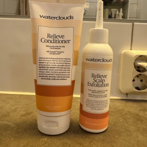 Relieve Conditioner och Relieve Scalp Exfoliation från Waterclouds - Två hårvårdsprodukter från Waterclouds: en Relieve Conditioner i tub och en Relieve Scalp Exfoliation i flaska med pipett. Båda har vita och orange toner och är anpassade för känslig hårbotten.