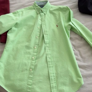 Ljusgrön skjorta från Polo Ralph Lauren - Snygg ljusgrön skjorta från Polo Ralph Lauren med klassisk button-down krage och broderad logga på bröstet. Skjortan har lång ärm och slim fit passform. Perfekt för dig som vill ha en stilren och fräsch look.