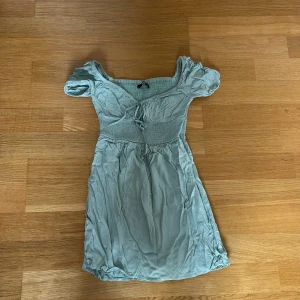 Ljusgrön kortklänning från Bik Bok - Supersöt ljusgrön klänning från Bik Bok med kort puffärm och smockad överdel. Klänningen har en feminin passform och är perfekt för varma dagar. Mjuk och lätt i materialet, med fina detaljer vid bysten.