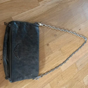 Svart axelväska från Zadig & Voltaire - Säljer en svart axelväska från Zadig & Voltaire i skinn med silverfärgad kedja som axelrem. Väskan har dragkedja upptill och diskret logga framtill. Perfekt storlek för det viktigaste och har ett innerfack. Väskan är köpt på vinted, äkta