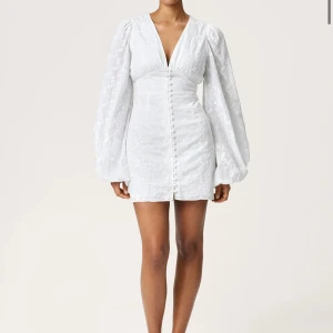 Adoore kortklänning med v-ringning och puffärmar - Säljer en snygg vit kortklänning med djup v-ringning och långa puffärmar. Klänningen har knappar framtill och markerad midja för en feminin siluett. Perfekt för sommarens alla tillfällen!