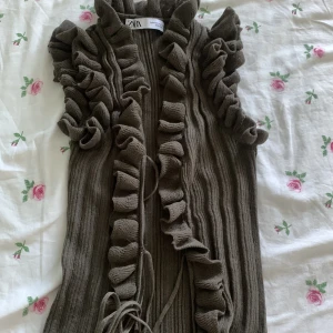 Grön ribbad kofta med volang från Zara - Supersöt grön top från Zara med volangdetaljer längs hela kanten och ärmarna. Koftan har knytband framtill och är perfekt för lager-på-lager. Snygg och trendig att styla till jeans eller kjol.