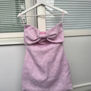 Rosa kort klänning med rosett - Söt rosa kort klänning med smala axelband och stor rosett framtill. Endast använd någongång!