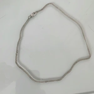 Silverfärgat halsband med kedjedesign - Säljer ett stilrent halsband i silverfärg med klassisk kedjedesign. Halsbandet har ett smidigt lås och passar perfekt för dig som gillar minimalistiska accessoarer. Enkelt att matcha med andra smycken.