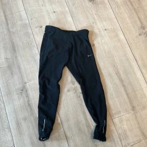 Svarta träningstights från Nike - Svarta träningstights från Nike med liten logga på låret och reflexdetaljer vid bensluten. Tight passform och stretchigt material som passar perfekt för löpning eller gym.