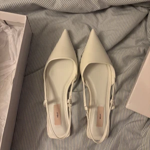 Vita pumps med spetsig tå från Nelly - Säljer ett par stilrena vita pumps från Nelly med spetsig tå och smala remmar runt hälen. Skorna har platt sula och är perfekta för dig som gillar minimalistisk och trendig design. HELT NYA, förpackning tillkommer!