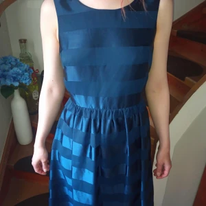 Marinblå randig klänning från Holly & Whyte - Säljer en marinblå klänning från Holly & Whyte med breda, horisontella ränder. Klänningen har rund halsringning, är ärmlös och har en markerad midja med lätt rynkad kjol. Dragkedja i sidan för enkel påklädning.