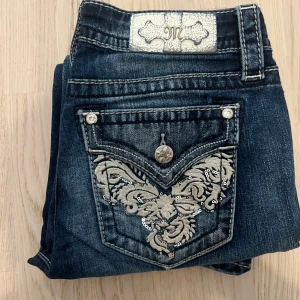 Miss Me Jeans med Vita Detaljer - Säljer ett par mörkblå jeans från Miss Me med snygga broderier och paljetter på bakfickorna. Jeansen har bootcut-modell och dekorativa knappar. Perfekta för dig som vill sticka ut med detaljer! Längd 105cm midja 36-38cm benöppning 22cm Knapp fattas. 