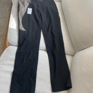 Svarta kostymbyxor från Bläck. Oanvända  - Säljer ett par svarta kostymbyxor från Black med klassisk rak passform. Byxorna har diskret dragkedja och knapp framtill. Perfekta för en stilren look och passar till många olika tillfällen. Nypris 799 kr
