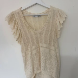 Virkad blus - Säljer en krämvit virkad  blus från Zara med v-ringning och korta volangärmar. Blusen har ett vackert stickat mönster och är perfekt för vår och sommar. Superfin att styla till både jeans och kjol