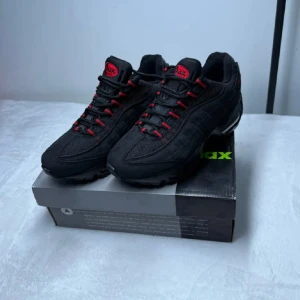 Nike Air Max 95 svart med röda detaljer - Säljer ett par svarta Nike Air Max 95 sneakers med röda detaljer och snörning. Skorna har en sportig design med synlig Air Max-dämpning i sulan och rund tå. Perfekta för dig som gillar streetwear och vill sticka ut med snygga kontraster. Och priset är inte hugget i sten 🪨 den är använt 2 gånger men tänkte sälja dom eftersom att dom va små för mig 