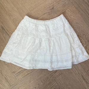 Vit kortkjol med mönster från Zara - Supersöt vit kortkjol från Zara med fina spetsdetaljer och broderade partier. Kjolen har resår i midjan och är perfekt för en fräsch sommarlook. Lätt och luftig modell som passar till många olika stilar.