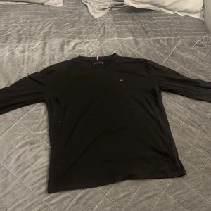Svart långärmad tröja från Tommy Hilfiger - Säljer en oanvänd svart långärmad tröja från Tommy Hilfiger. Tröjan har en klassisk passform och är tillverkad i mjuk bomull. Liten broderad logga på bröstet och rund halsringning. Perfekt för en stilren och enkel look.