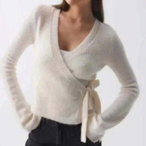 Vit omlottkofta med knytband - Snygg vit omlottkofta med knytband i sidan. Tröjan har lång ärm och är croppad, perfekt att styla över ett linne eller topp. Mjuk och skön känsla, passar till många olika outfits.