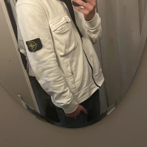 Stone Island - Säljer en vit zip kofta från Stone Island med klassisk logotyp-patch på vänster ärm. Jackan har tett stora bröstficka. Perfekt för dig som gillar en avslappnad luck och vill ha något stilrent.