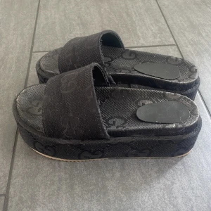 Svarta platåsandaler - Säljer ett par svarta platåsandaler med bred rem. Skorna har öppen tå och plattformsula, perfekta för sommaren. Snygga och trendiga att bära till både jeans och klänning. 