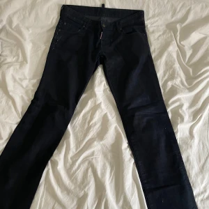 Svarta jeansbyxor från Dsquared2 - Säljer ett par svarta jeansbyxor från Dsquared2. Klassisk femficksmodell med raka ben och diskreta detaljer. Jeansen har knappgylf och Dsquared2-logga på bakfickan. Perfekta för dig som gillar stilrena och exklusiva jeans.