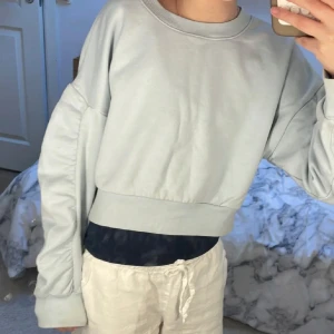 Ljusblå croppad sweatshirt från Lindex - Säljer en ljusblå croppad sweatshirt från Lindex. Tröjan har rund halsringning, långa ärmar med breda muddar och en bred resår i nederkanten. Perfekt för en avslappnad och trendig look.