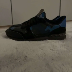 Valentino Rockrunner sneakers med blå kamouflage - Säljer ett par Valentino Rockrunner sneakers med blått och svart kamouflagemönster. Skorna har svarta snören, rund tå och detaljer i skinn och mocka. Snygg och unik design med blå häl och klassisk Valentino-logga på plösen. Du får även med dustbag och extra snören😇