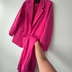 Kostym i starkt rosa från bikbok - Säljer en tvådelad kostym från bikbok i en stark rosa färg. Kavajen har klassisk krage, knappar framtill och fickdetaljer. Byxorna är raka och matchar kavajen perfekt. Perfekt för dig som vill sticka ut!