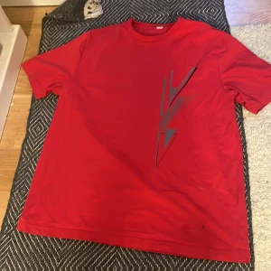 Röd t-shirt med grafiskt tryck - Röd t-shirt med svart grafiskt tryck på framsidan. Klassisk rund halsringning och korta ärmar. Perfekt för en avslappnad stil. Inte använt en enda gång 