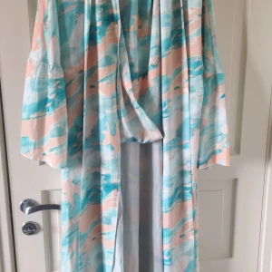 Pastellfärgad långklänning från SHEIN - Säljer en flowy långklänning från SHEIN med pastelliga blå, rosa och beige toner. Klänningen har vida ärmar och ett abstrakt mönster som ger en soft och chill vibe. Perfekt för varma dagar eller när du vill sticka ut lite extra.