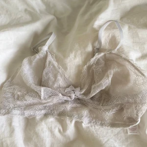 Vit spets bralette från Dorina - Säljer en vit bralette från Dorina i mjuk spets med tunna axelband och liten rosett framtill. Toppen är ärmlös och har ett romantiskt spetsmönster över hela ytan. Perfekt för dig som gillar feminina detaljer.