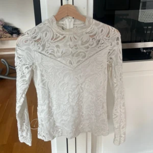 Vit spetsblus med lång ärm från vila  - Säljer en elegant vit blus i spets med lång ärm och rund halsringning. Blusen har ett vackert mönster och transparenta partier upptill. Perfekt för dig som vill ha en romantisk och stilren look.