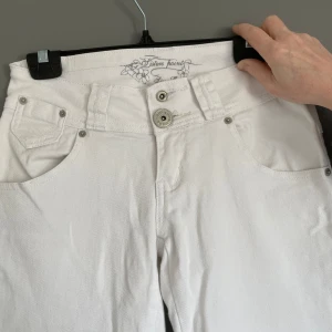 Vita jeansbyxor  - Vita jeansbyxor från Silver Point med raka ben. Dem är uppsydda vid insidan av byx kanten längst ner på byxorna, där av fransiga, inget som syns utåt! Byxorna har dubbla knappar fram, dekorativa nitar och detaljerade bakfickor. Klassisk femficksmodell med normal passform och mid midja.