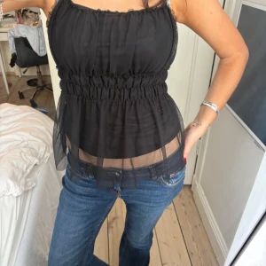 Svart transparent linnetopp med resår - Säljer en svart, transparent linnetopp med smala axelband och resår i midjan. Toppen har en luftig och flowy passform med dubbla lager tyg och lätt rynkade detaljer. Perfekt att styla över ett linne eller bh.