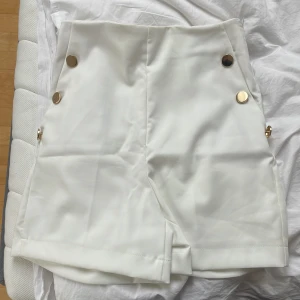 Vita shorts från LCW CASUAL - Stilrena vita shorts med hög midja och dekorativa guldknappar framtill. Shortsen har en dold dragkedja i sidan och uppvikta benslut för en snygg finish. Perfekta för en trendig och elegant look.
