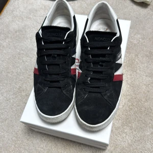 Moncler Monaco M sneakers herr 44 - Säljer ett par Moncler Monaco M sneakers i svart mocka med vita och röda detaljer. Skorna har snörning, vit sula och rund tå. Klassisk Moncler-logga på hälen och vit insida. Perfekta för dig som gillar stilrena och liknande de andra alternativen när de kommer till skor, men lite annorlunda på samma gång. Nypris: 5000-6000 köpt på NK Göteborg. 