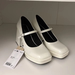 Vita Mary Jane pumps med platå och klack - Säljer ett par vita Mary Jane pumps från Monki med bred fyrkantig klack och platåsula. Skorna har en smal rem över foten och rund tå. Perfekta för dig som gillar statementskor med retrovibbar.