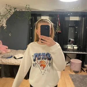 Vit sweatshirt med baskettryck - Vit sweatshirt med stort basketinspirerat tryck i blått och orange framtill. Använd enstaka gång då jag inte riktigt fastnat för trycket!